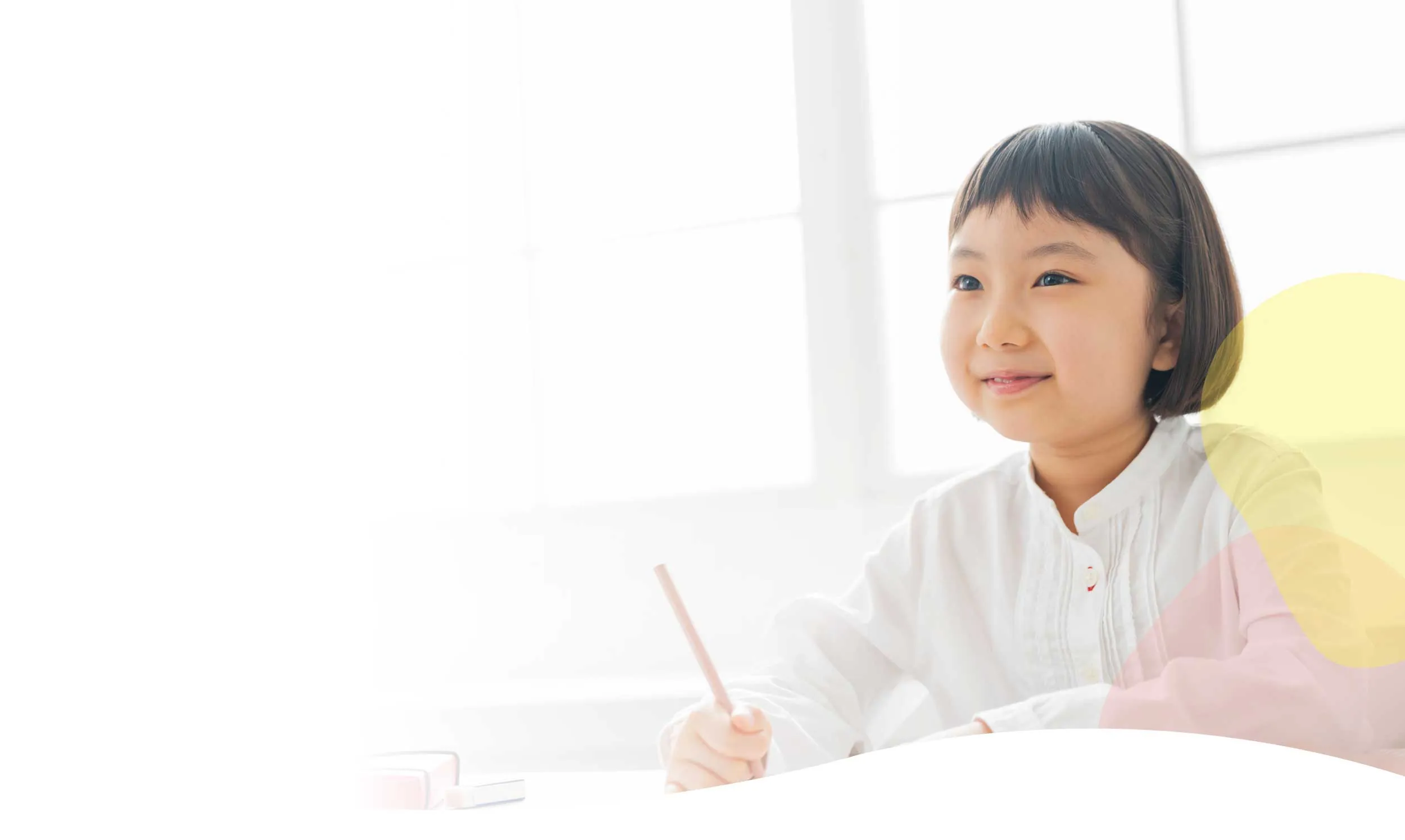 机で鉛筆を持ち、考えながらほほ笑む子ども